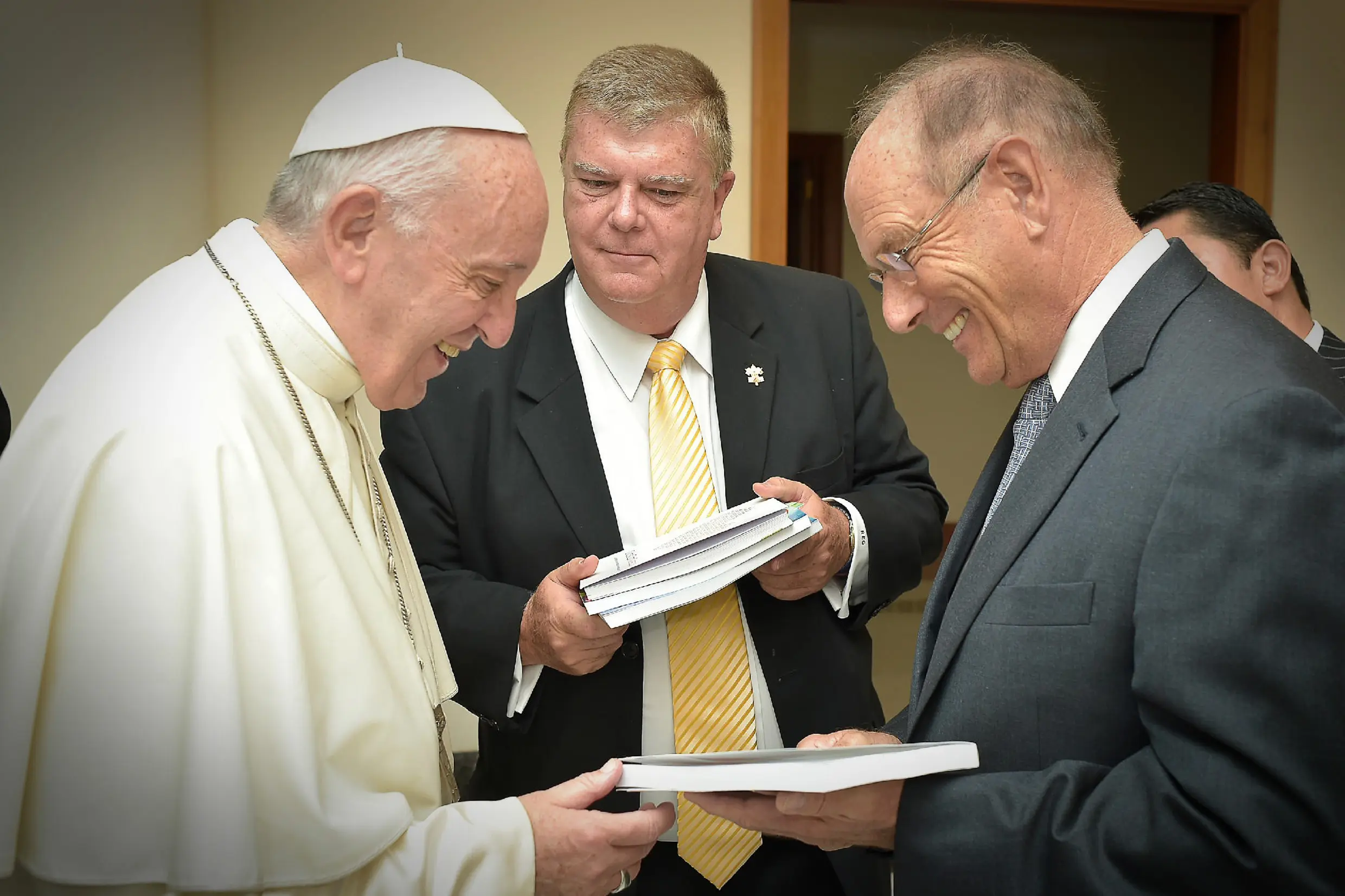 Pope Francis lauging with two men presenting him books.